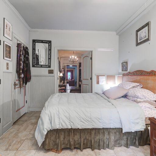 81 Rutledge Ave, Charleston, SC 29401 - bedroom with a chandelier, crown molding, light tile patterned flooring, and a wainscoted wall