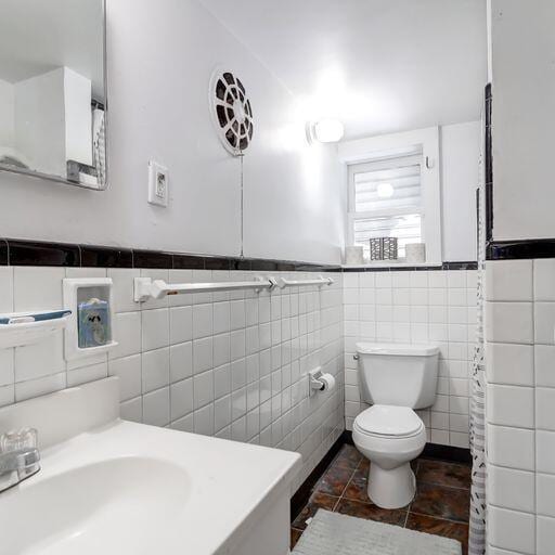 81 Rutledge Ave, Charleston, SC 29401 - bathroom featuring a sink, toilet, tile walls, tile patterned flooring, and wainscoting