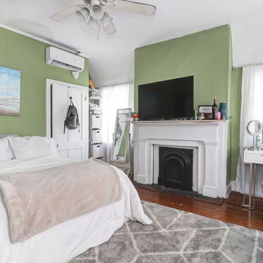 81 Rutledge Ave, Charleston, SC 29401 - bedroom with a wall mounted AC, wood finished floors, a ceiling fan, and a fireplace with flush hearth