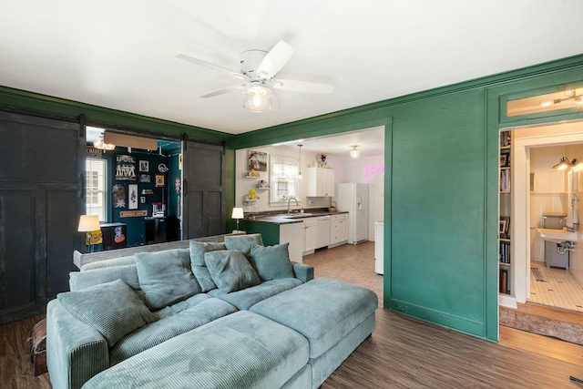 living area with a ceiling fan, wood finished floors, and a barn door