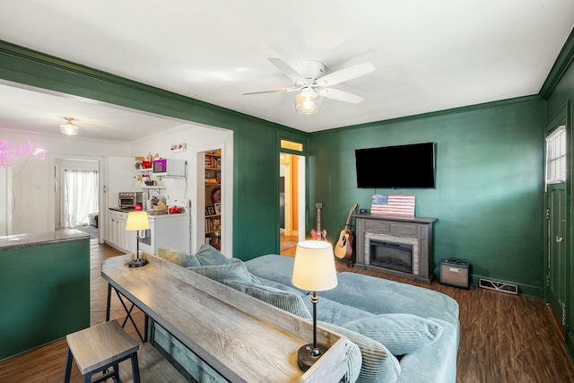 living room featuring visible vents, ceiling fan, wood finished floors, crown molding, and a fireplace