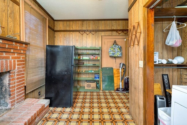 kitchen featuring tile counters, a brick fireplace, black fridge, wood walls, and washer / dryer