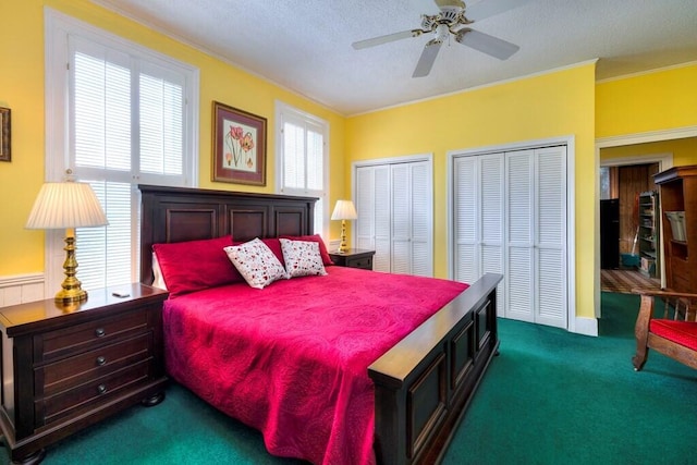 bedroom with a textured ceiling, ceiling fan, crown molding, dark colored carpet, and multiple closets