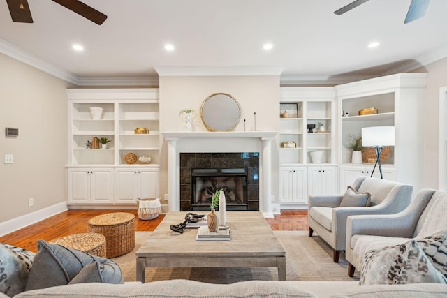 living room featuring light wood-style flooring, a fireplace, ornamental molding, and a ceiling fan