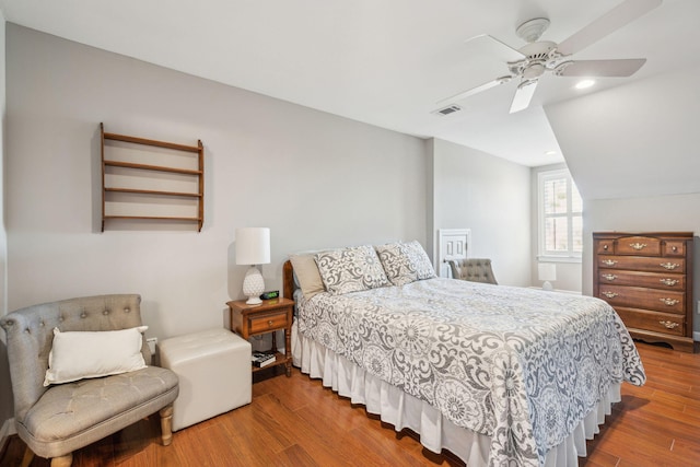 bedroom featuring a ceiling fan, visible vents, vaulted ceiling, and wood finished floors