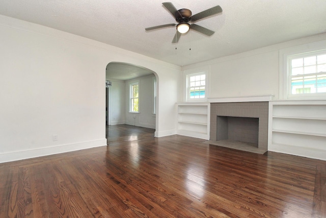 unfurnished living room with dark hardwood / wood-style flooring, a textured ceiling, ceiling fan, built in features, and a fireplace