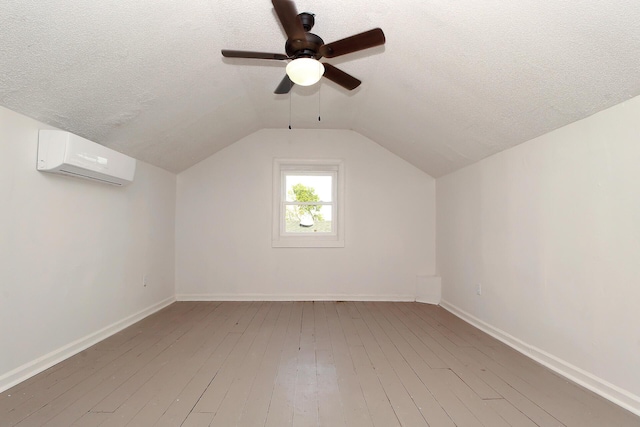 bonus room featuring a textured ceiling, a wall mounted AC, lofted ceiling, and light wood-type flooring