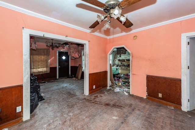 interior space with ceiling fan, wooden walls, crown molding, and wainscoting