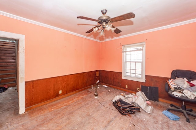 unfurnished room featuring a wainscoted wall, wooden walls, ornamental molding, and a ceiling fan