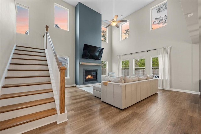 living area featuring a glass covered fireplace, stairway, wood finished floors, and baseboards