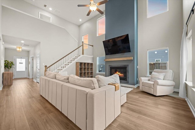 living area featuring light wood-type flooring, a glass covered fireplace, stairway, and a high ceiling