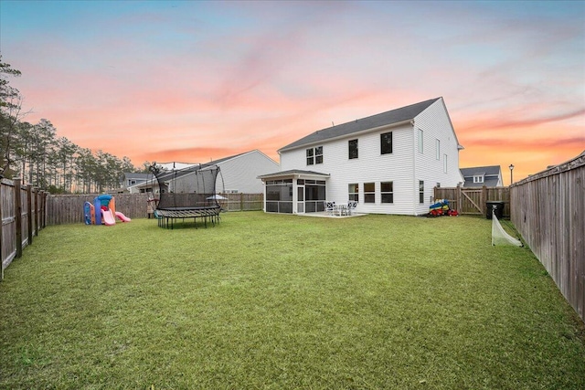 217 Lucca Dr, Summerville, SC 29486 - back of house at dusk featuring a sunroom, a fenced backyard, a trampoline, and a yard