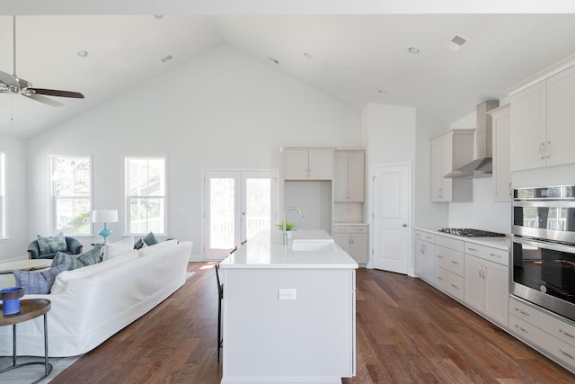 kitchen with white cabinetry, dark wood-type flooring, appliances with stainless steel finishes, a center island with sink, and wall chimney range hood