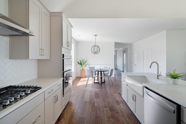 kitchen with appliances with stainless steel finishes, wall chimney exhaust hood, backsplash, hanging light fixtures, and dark hardwood / wood-style floors