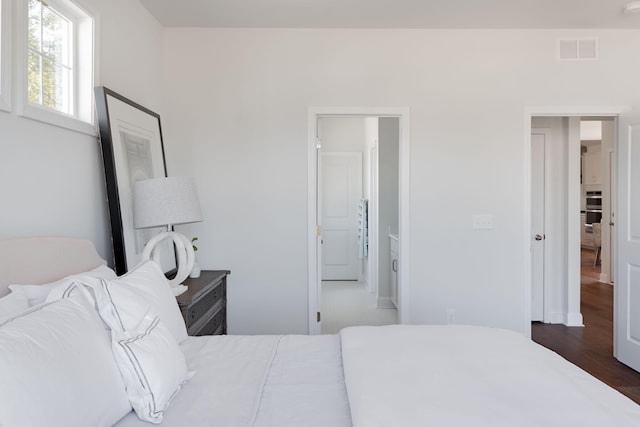bedroom with ensuite bathroom and dark wood-type flooring