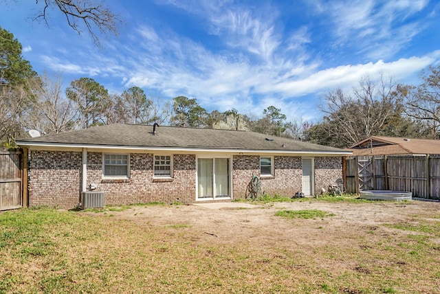 back of property with brick siding, central AC unit, a lawn, and fence