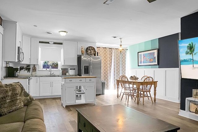 kitchen featuring a wainscoted wall, a sink, light wood-style floors, appliances with stainless steel finishes, and white cabinets