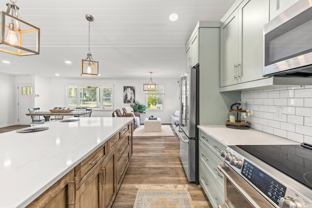 kitchen with wood finished floors, recessed lighting, hanging light fixtures, appliances with stainless steel finishes, and backsplash