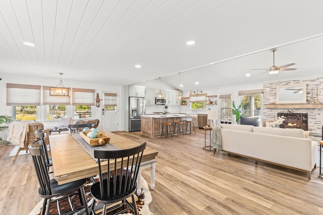 dining space with recessed lighting, a brick fireplace, light wood-type flooring, and vaulted ceiling