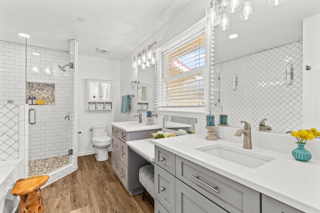 bathroom featuring toilet, two vanities, a stall shower, wood finished floors, and a sink