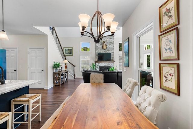 dining space featuring a fireplace, dark wood-type flooring, stairway, a chandelier, and baseboards