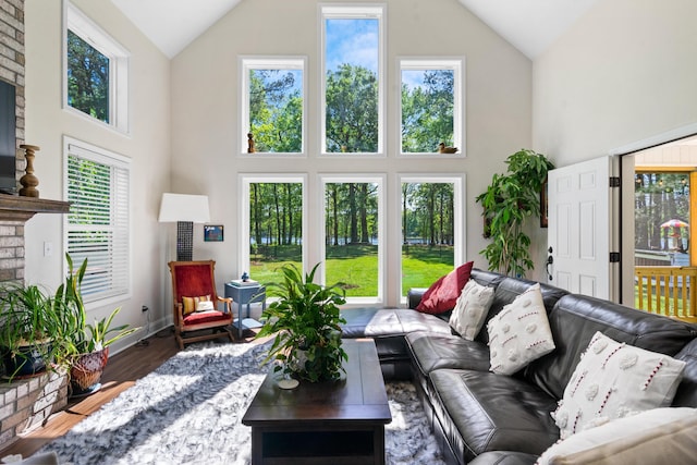 living room featuring baseboards, high vaulted ceiling, a brick fireplace, and wood finished floors