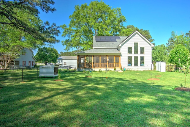 rear view of property with a shingled roof, a sunroom, a lawn, and roof mounted solar panels