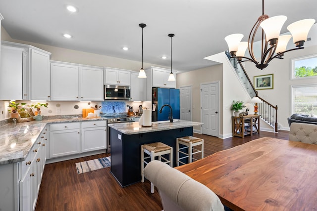 kitchen with dark wood-style flooring, appliances with stainless steel finishes, white cabinetry, and light stone countertops