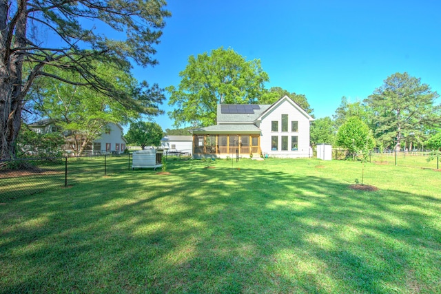 back of house featuring a fenced backyard, a sunroom, a lawn, and roof mounted solar panels