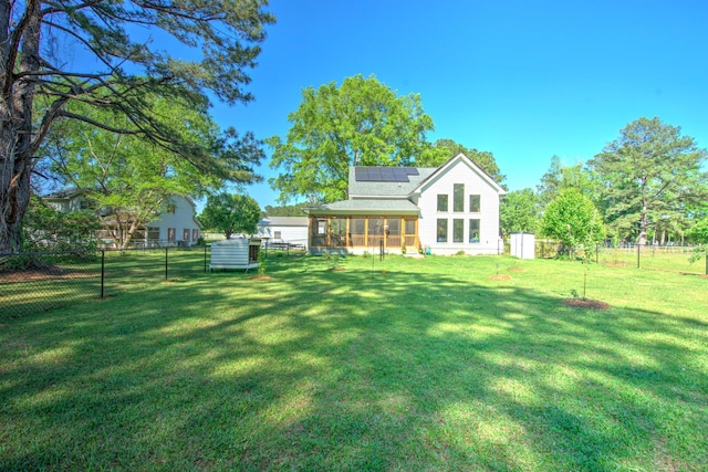 rear view of property with a sunroom, a yard, fence, and solar panels