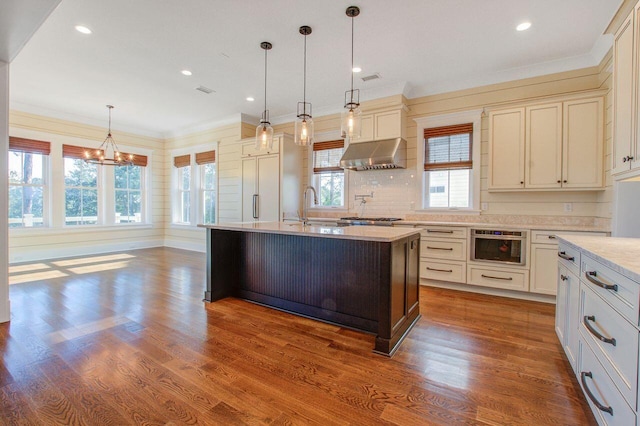 kitchen featuring ventilation hood, wood-type flooring, a center island with sink, and hanging light fixtures