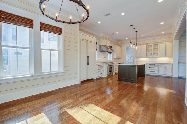 kitchen featuring extractor fan, stainless steel stove, a center island with sink, hardwood / wood-style floors, and pendant lighting