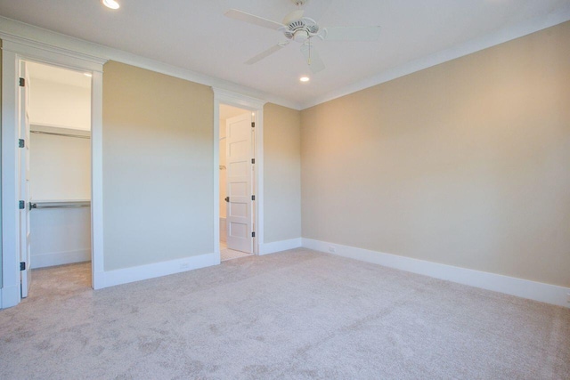 unfurnished bedroom with a closet, light carpet, a spacious closet, crown molding, and ceiling fan