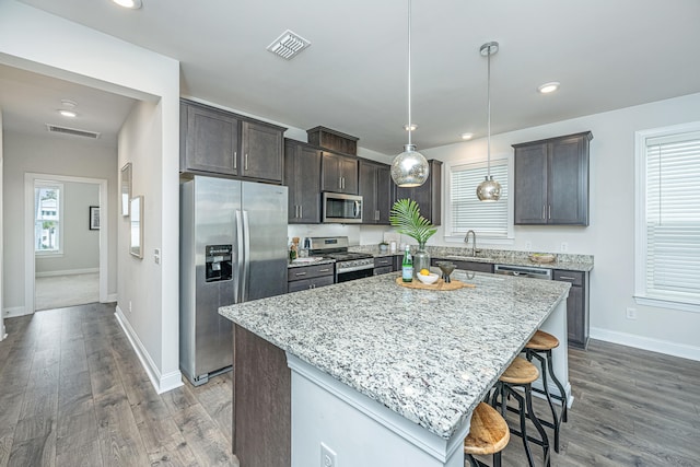 kitchen featuring stainless steel appliances, decorative light fixtures, a kitchen bar, and a kitchen island