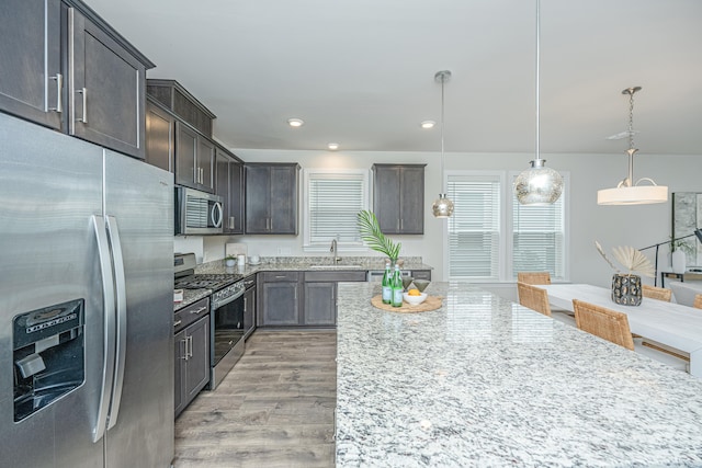 kitchen with sink, hanging light fixtures, stainless steel appliances, a center island, and light hardwood / wood-style floors