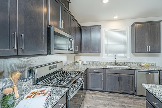 kitchen with appliances with stainless steel finishes, sink, light hardwood / wood-style floors, light stone countertops, and dark brown cabinets