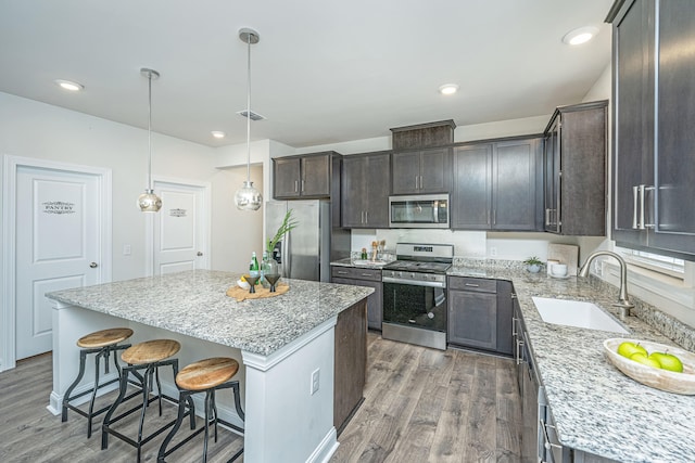 kitchen with pendant lighting, sink, hardwood / wood-style flooring, stainless steel appliances, and a kitchen island