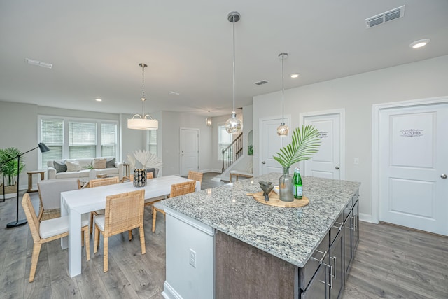 kitchen featuring hanging light fixtures, a center island, light stone counters, and light wood-type flooring