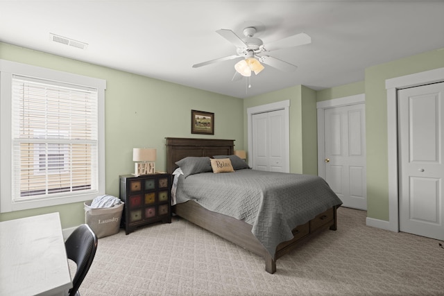 bedroom with ceiling fan, light colored carpet, visible vents, baseboards, and two closets