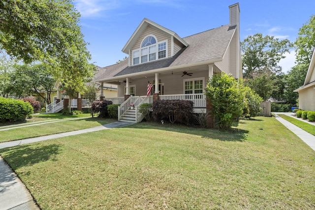 view of front facade with a ceiling fan, a front lawn, covered porch, and a shingled roof