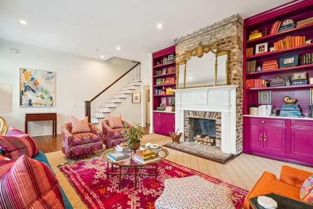 living room with built in features, light hardwood / wood-style floors, and a brick fireplace