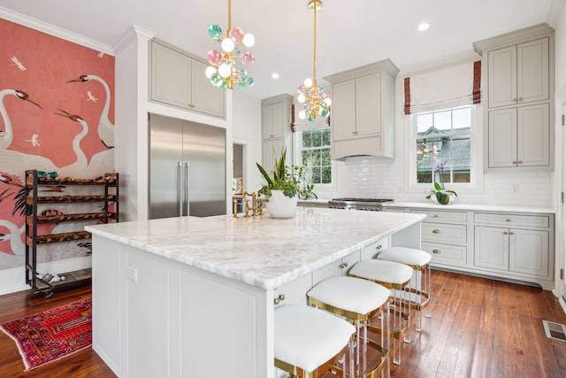 kitchen with dark wood-type flooring, built in fridge, decorative backsplash, decorative light fixtures, and a kitchen island