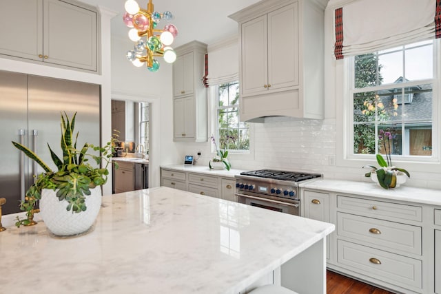 kitchen featuring backsplash, a wealth of natural light, light stone countertops, and high end appliances