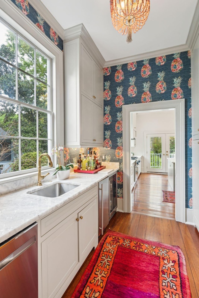 interior space featuring sink, light hardwood / wood-style flooring, stainless steel dishwasher, ornamental molding, and white cabinetry