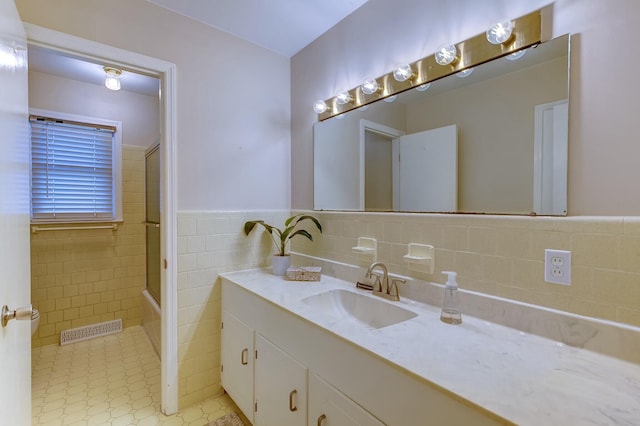 full bath with visible vents, combined bath / shower with glass door, tile walls, wainscoting, and vanity