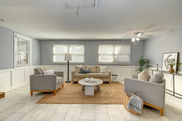 living area with a wainscoted wall, attic access, a ceiling fan, and a decorative wall