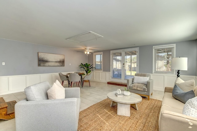 living room featuring light tile patterned floors, attic access, wainscoting, and a decorative wall