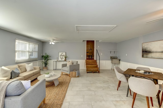 living room with stairway, wainscoting, attic access, and ceiling fan