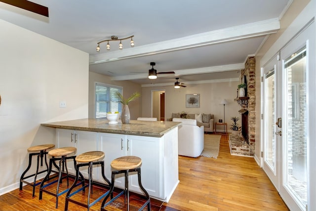 kitchen featuring a peninsula, light wood-style flooring, stone countertops, ceiling fan, and beamed ceiling