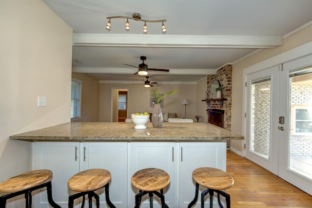 kitchen with light stone countertops, light wood finished floors, a peninsula, ceiling fan, and white cabinets